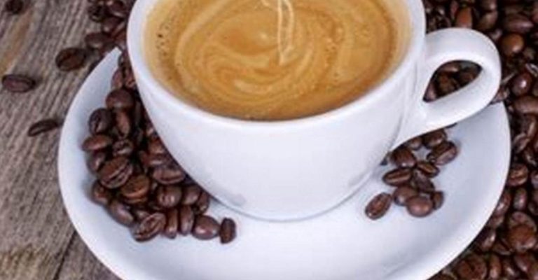 Tasse de café crémeux entourée de grains de café sur une table en bois.