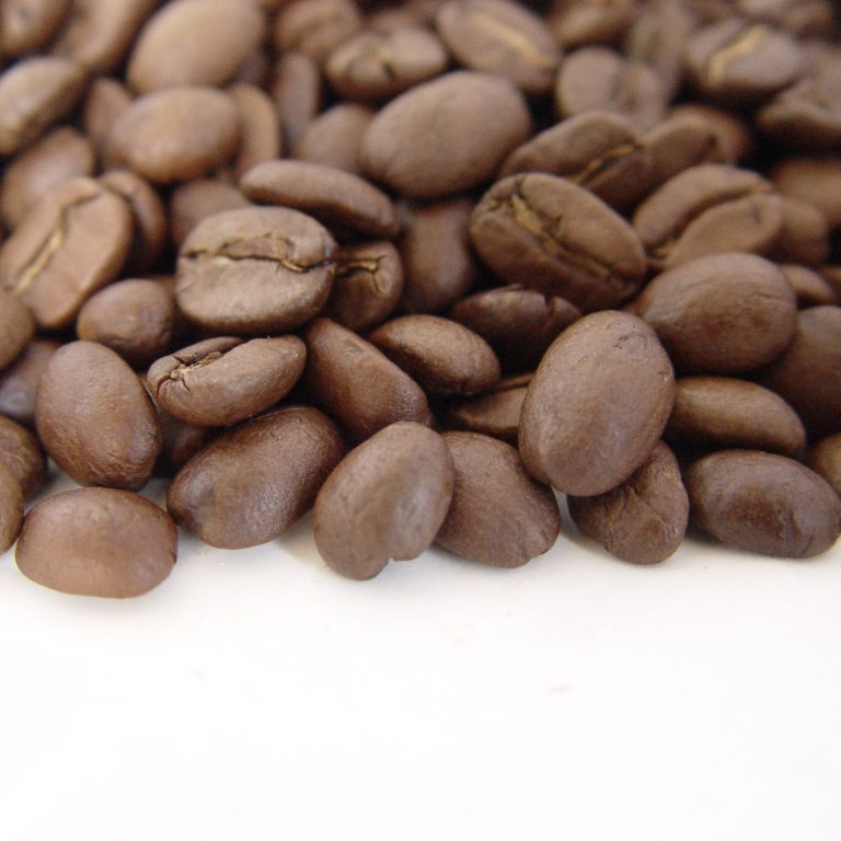 Grains de café bruns, en tas, avec des reflets brillants.